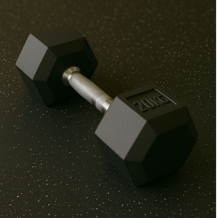 A 20kg hexagonal dumbbell with a textured silver handle rests on a speckled black rubber gym floor, positioned diagonally with clear weight marking visible.