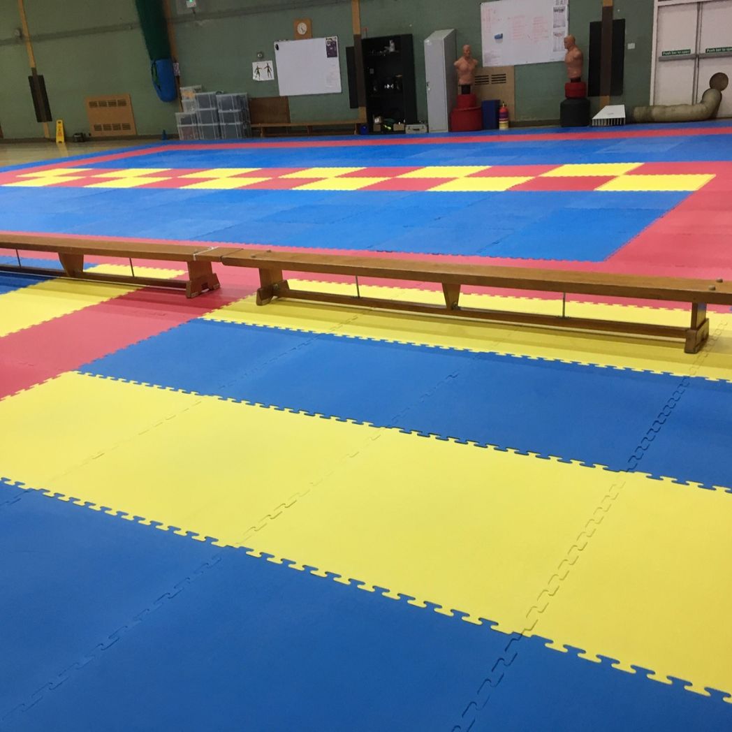 Yellow and blue interlocking tatami mats laid out in a gymnastics hall.