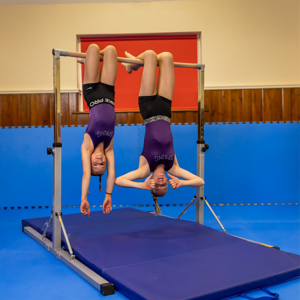 Lifestyle: two young gymnasts training on the pink junior bar — technique work and drills