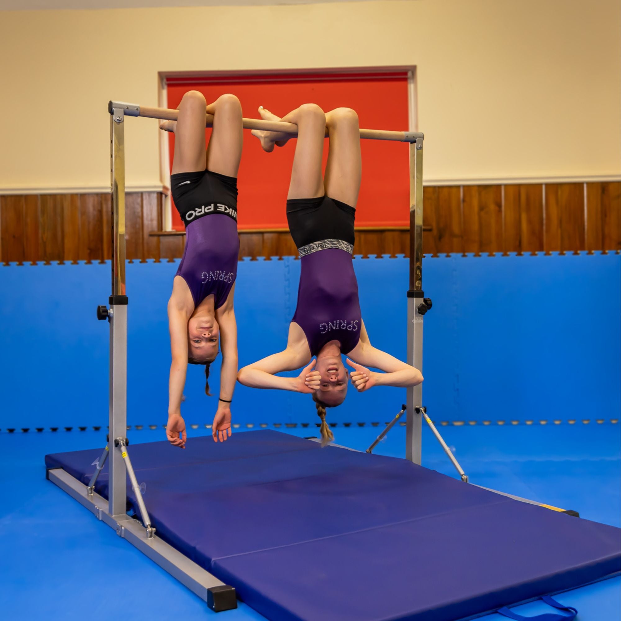 Lifestyle: two young gymnasts training on the pink junior bar — technique work and drills