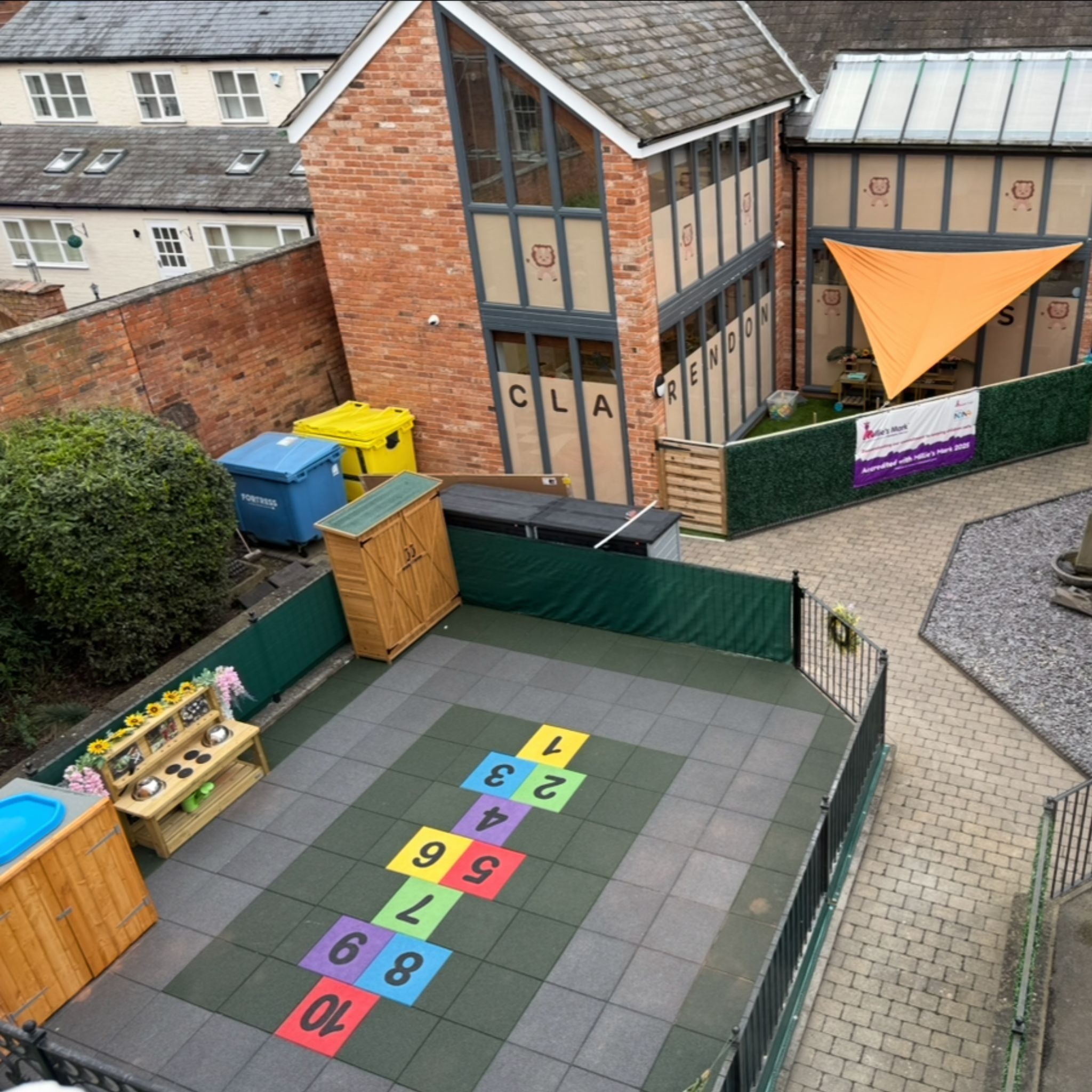 Outdoor area with colorful hopscotch grid on tiled surface, surrounded by buildings.