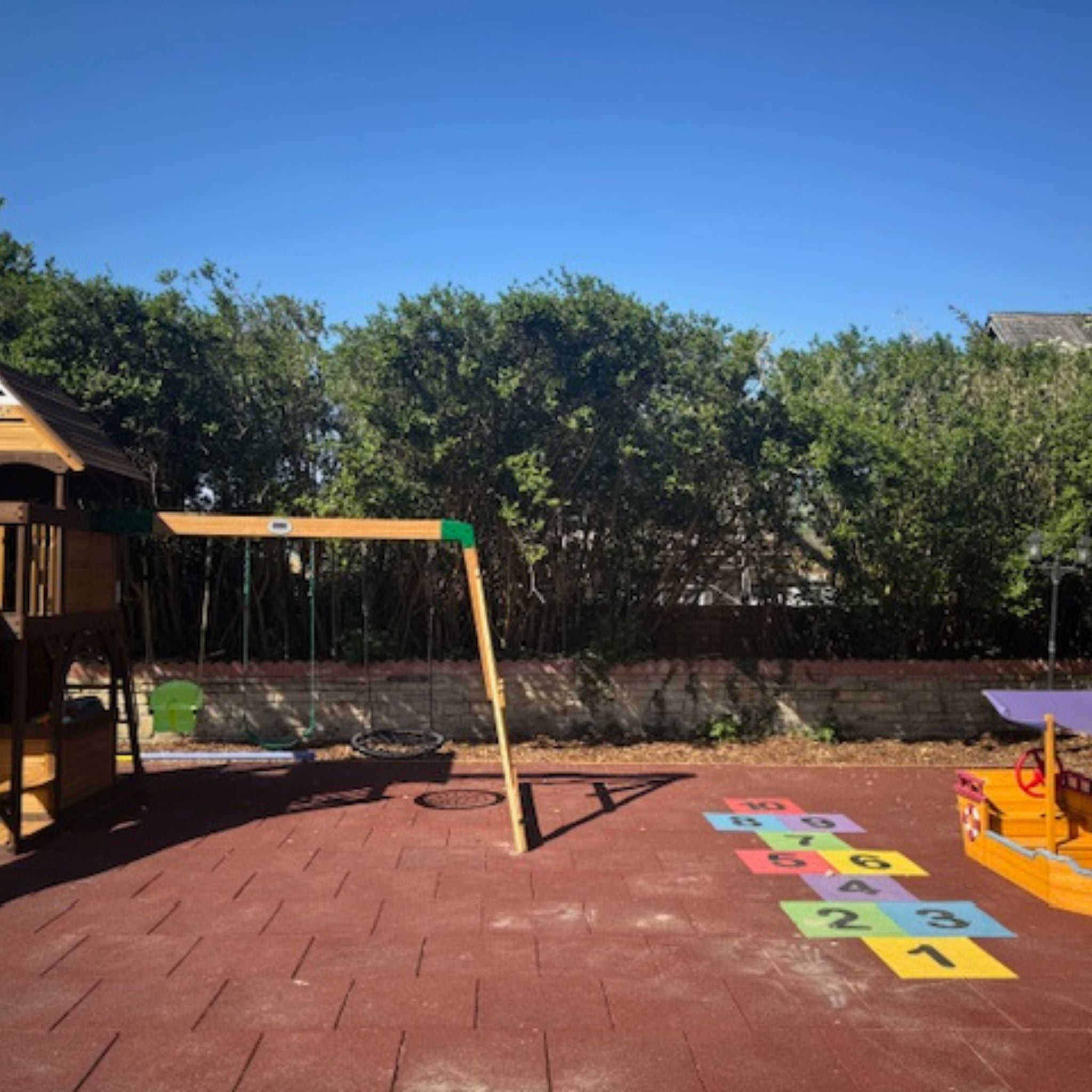 Children's playground with swing set and colorful hopscotch grid on red brick surface.