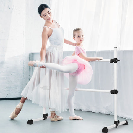Child stretching on freestanding white ballet barre in studio  
